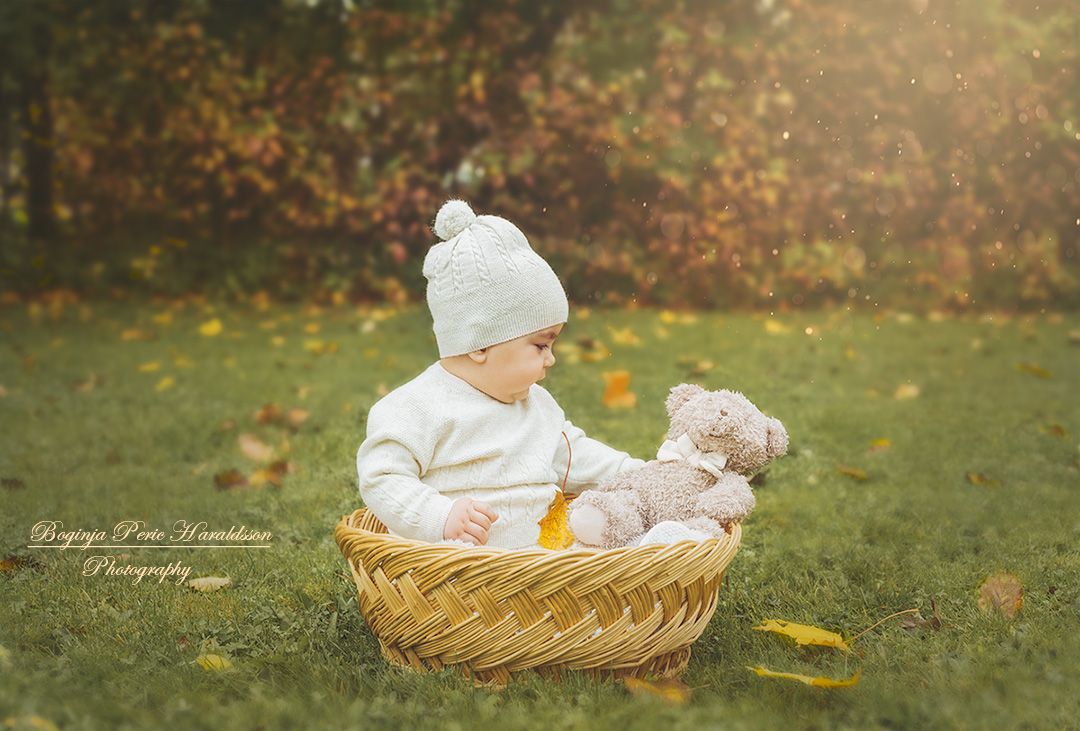 Barn sitter i en liten korg och leker med sin nalle.