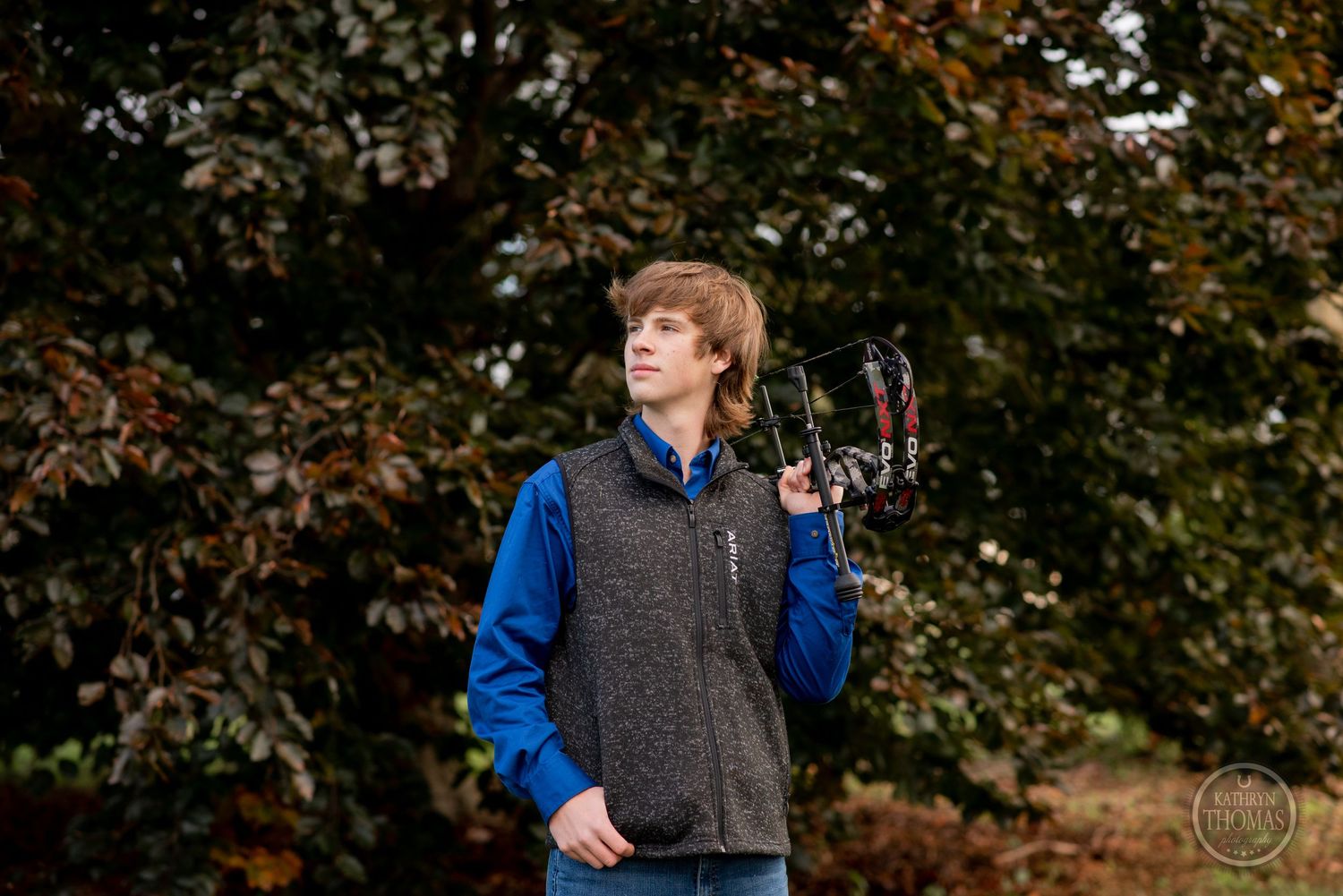 Someone holds up a compound bow while wearing casual outdoor attire.
