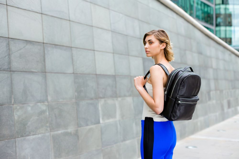 Athletic wear paired with black leather backpack against urban wall.
