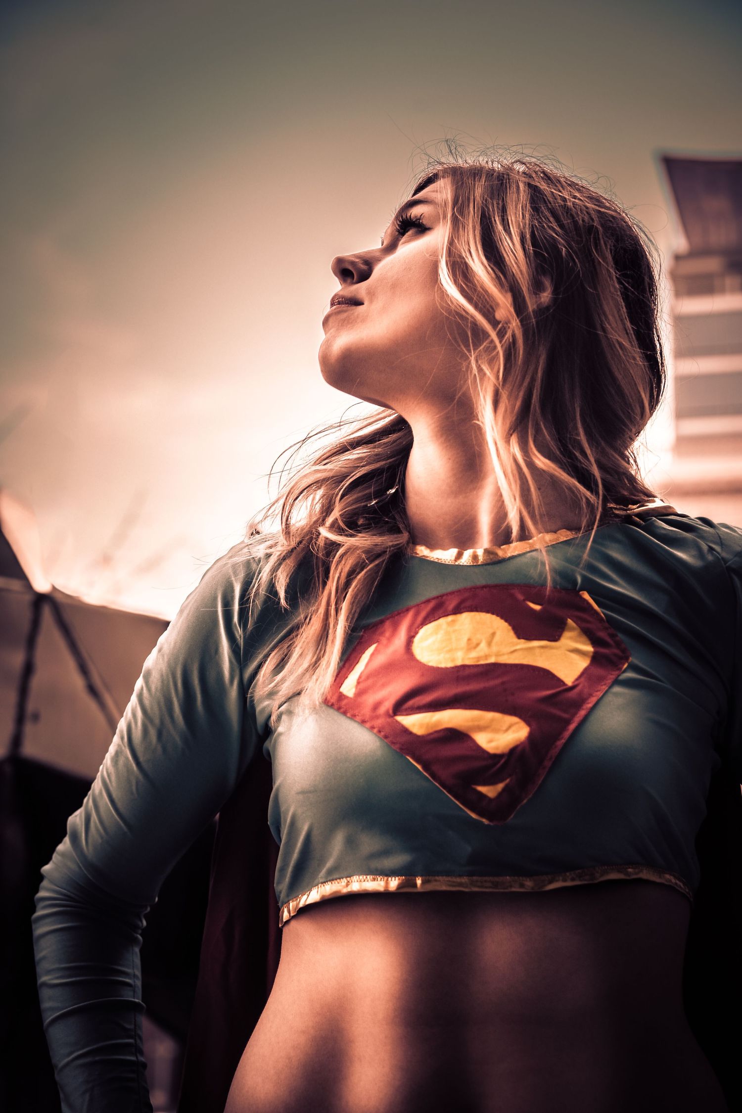 Artistic portrait of Supergirl cosplay with dramatic lighting and upward angle.