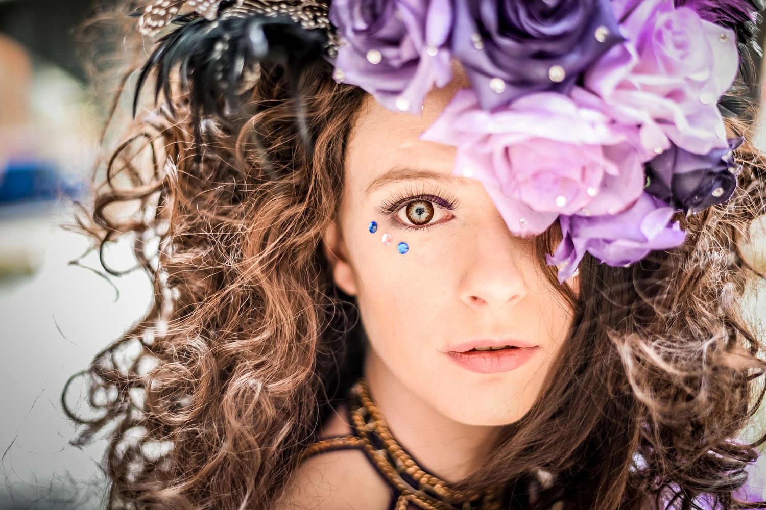 Portrait with curly hair adorned with purple and pink flowers against a blurred background.