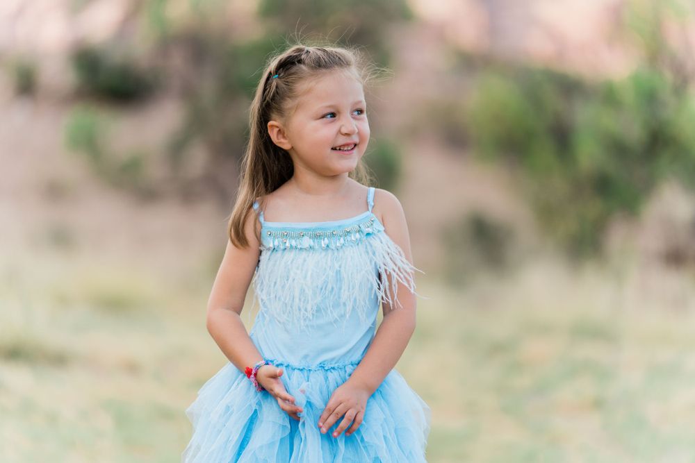 A child in a light blue tulle dress twirls joyfully in a sunny outdoor setting.