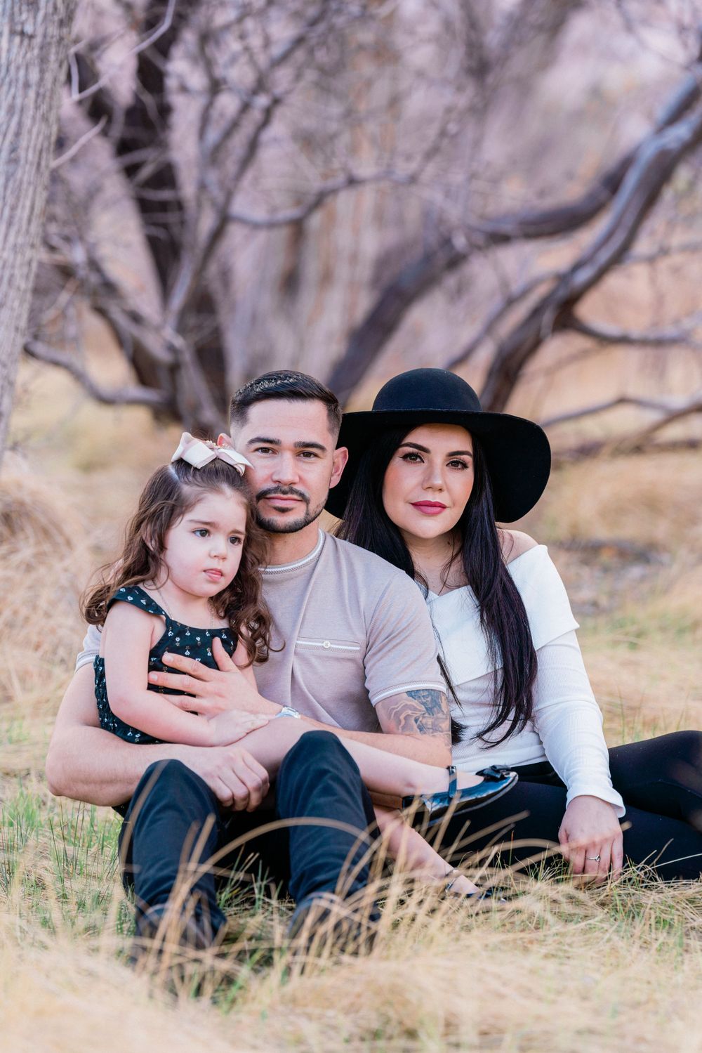 A family sits together in tall grass with bare trees and mountains in the background.