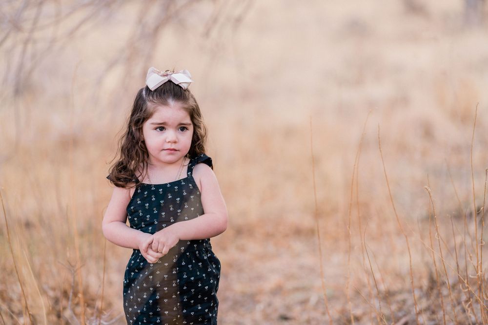 A young child in a polka dot dress stands in a field of golden grass.