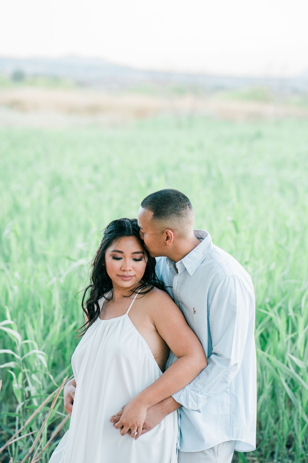 Couple in white outfits share intimate moments in a lush green field.