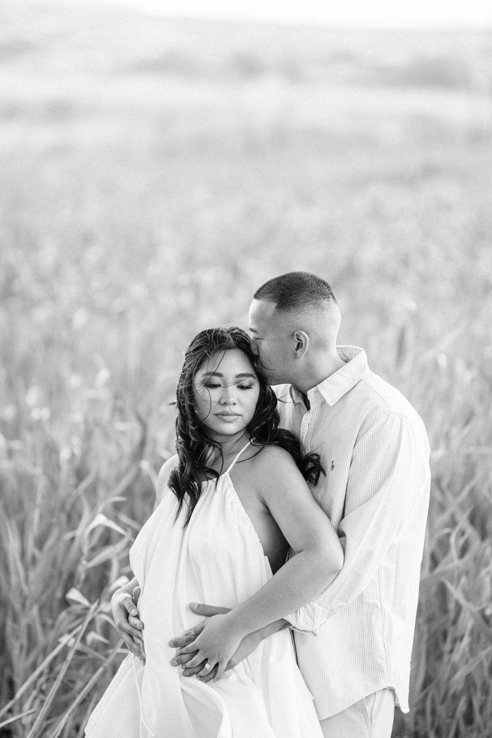 Romantic couple embraces in a serene wheat field during a black and white photoshoot.