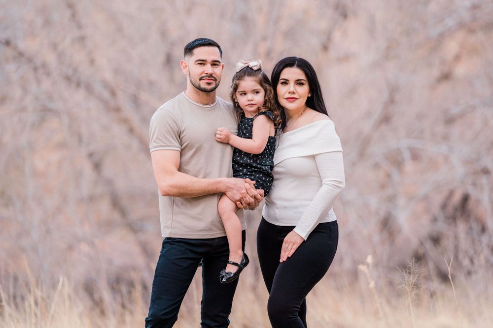 A family of three poses together outdoors against a desert mountain backdrop.
