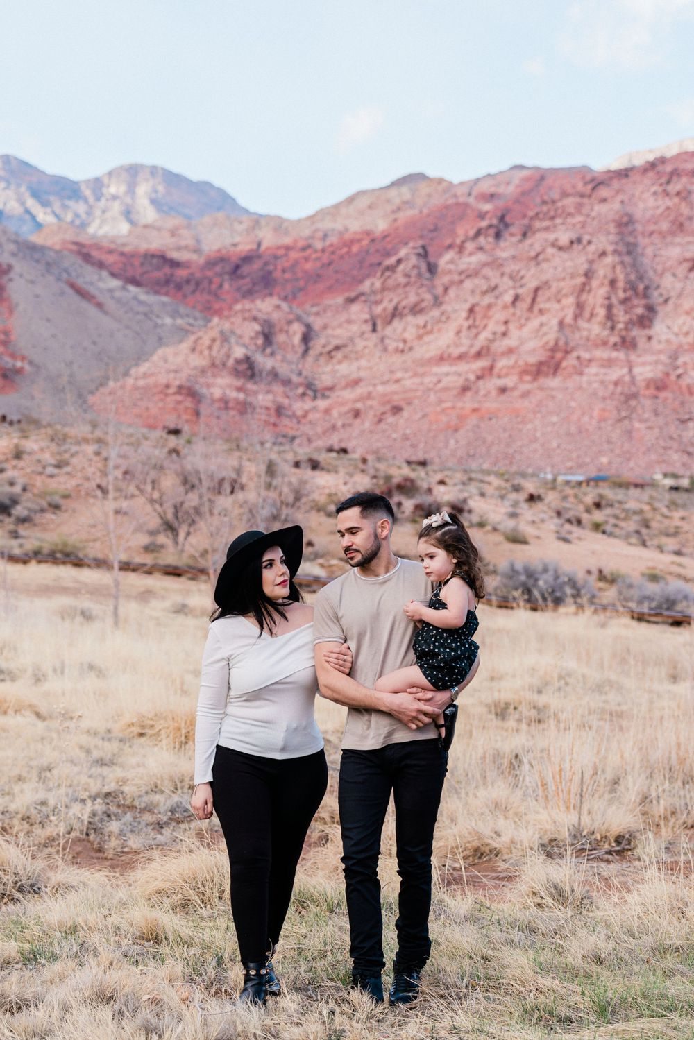 A family stands together against stunning red rock mountains in a desert landscape.