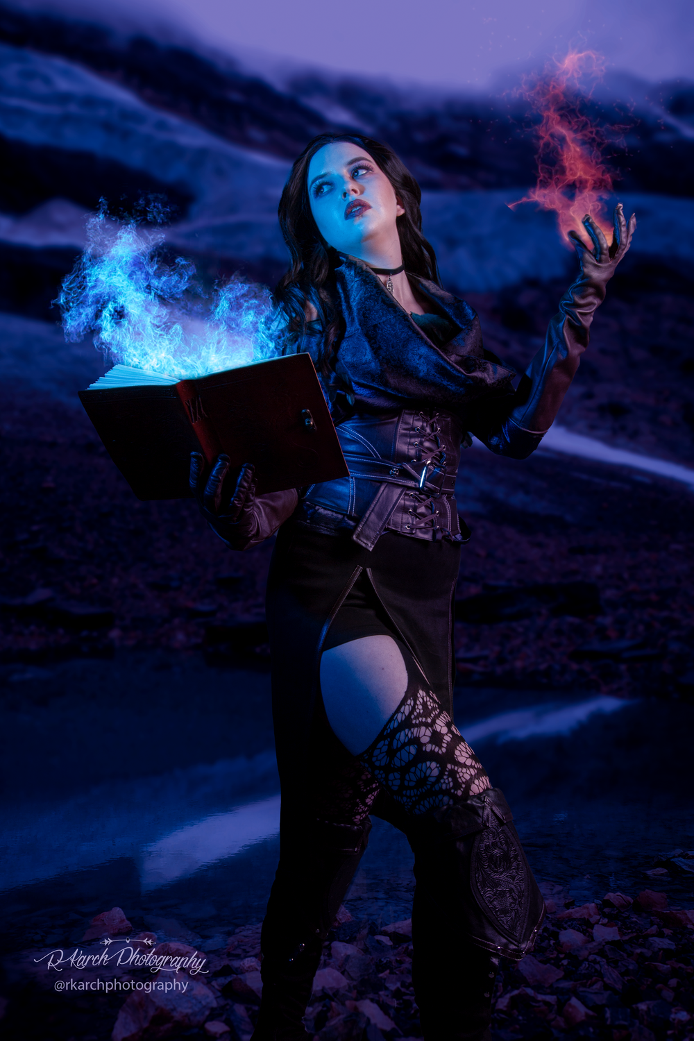 Gothic sorceress casting blue magic while holding spellbook in nighttime scene.