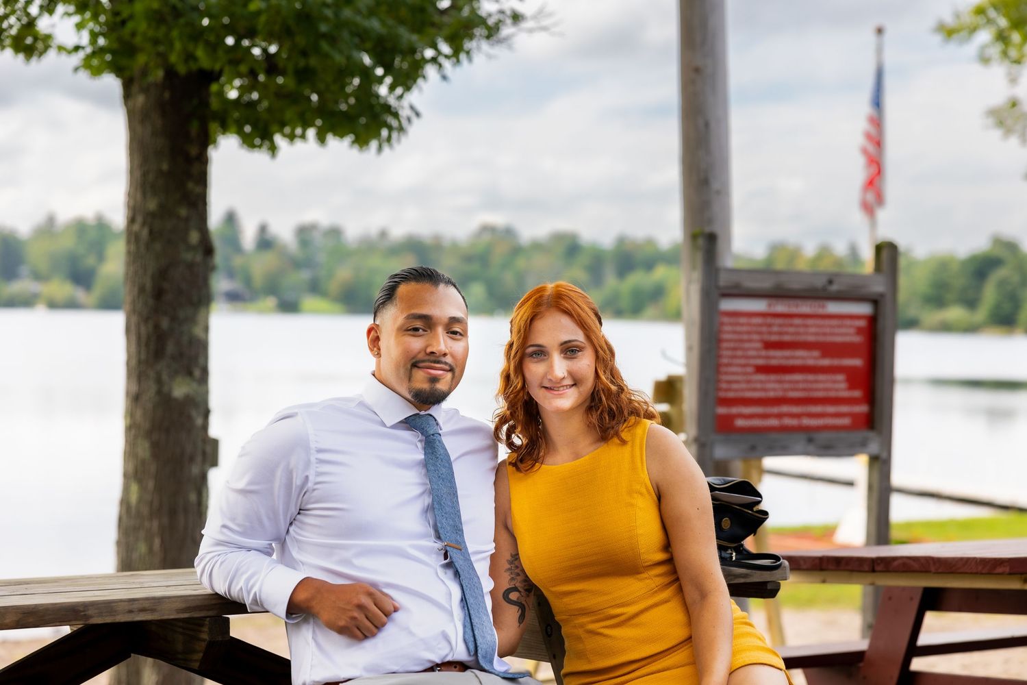 Outdoor waterfront venue with trees and American flags visible in background on sunny day.