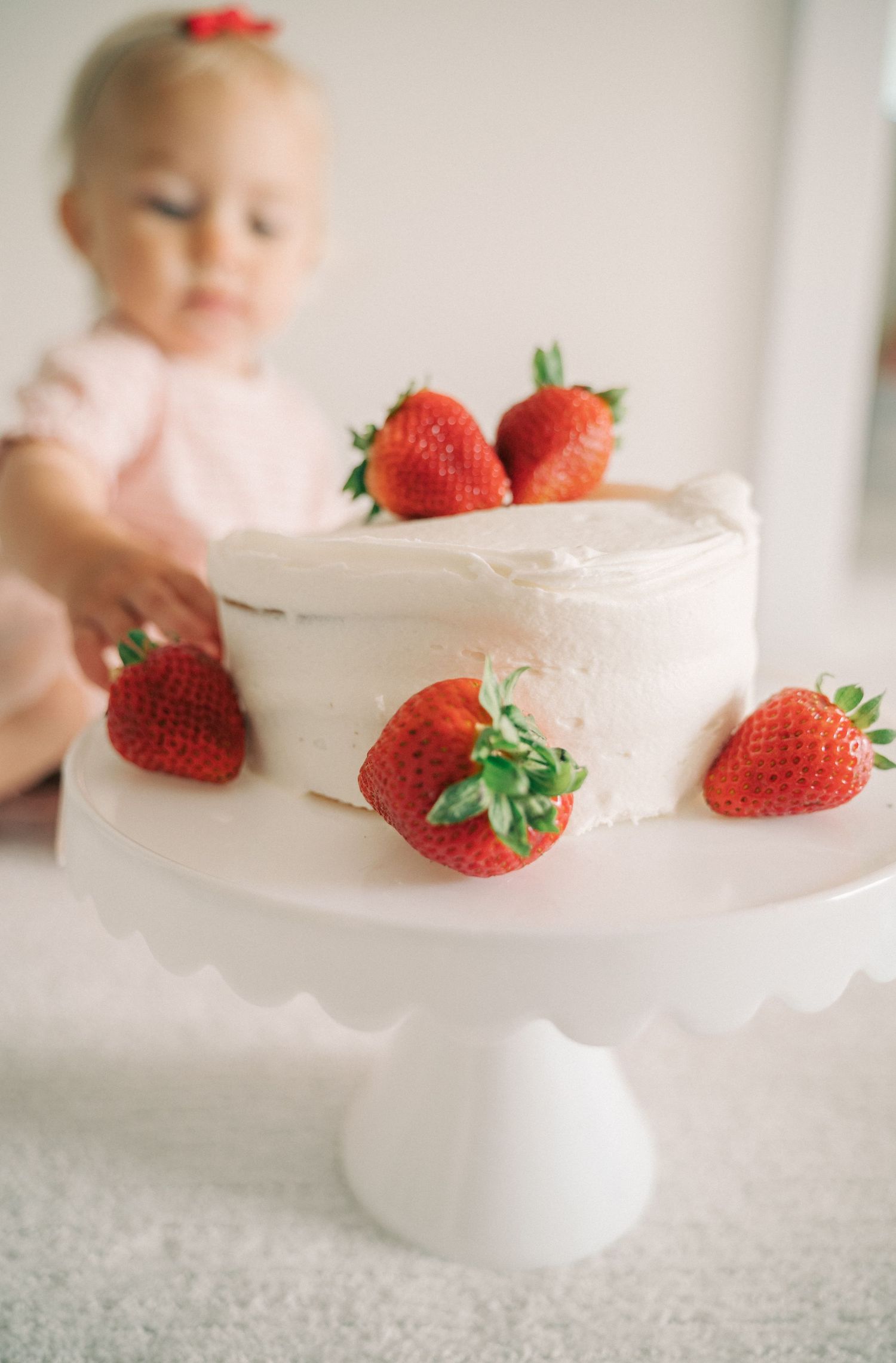 A two-tiered white cake decorated with fresh red strawberries on a pedestal cake stand.