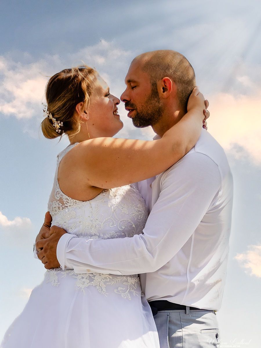 Two people share an intimate moment at sunset in formal wedding attire.