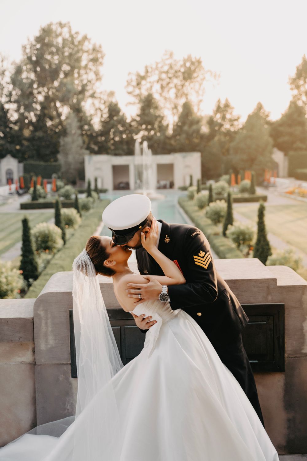 Romantic sunset wedding photo of military groom dipping bride in white gown for a kiss.
