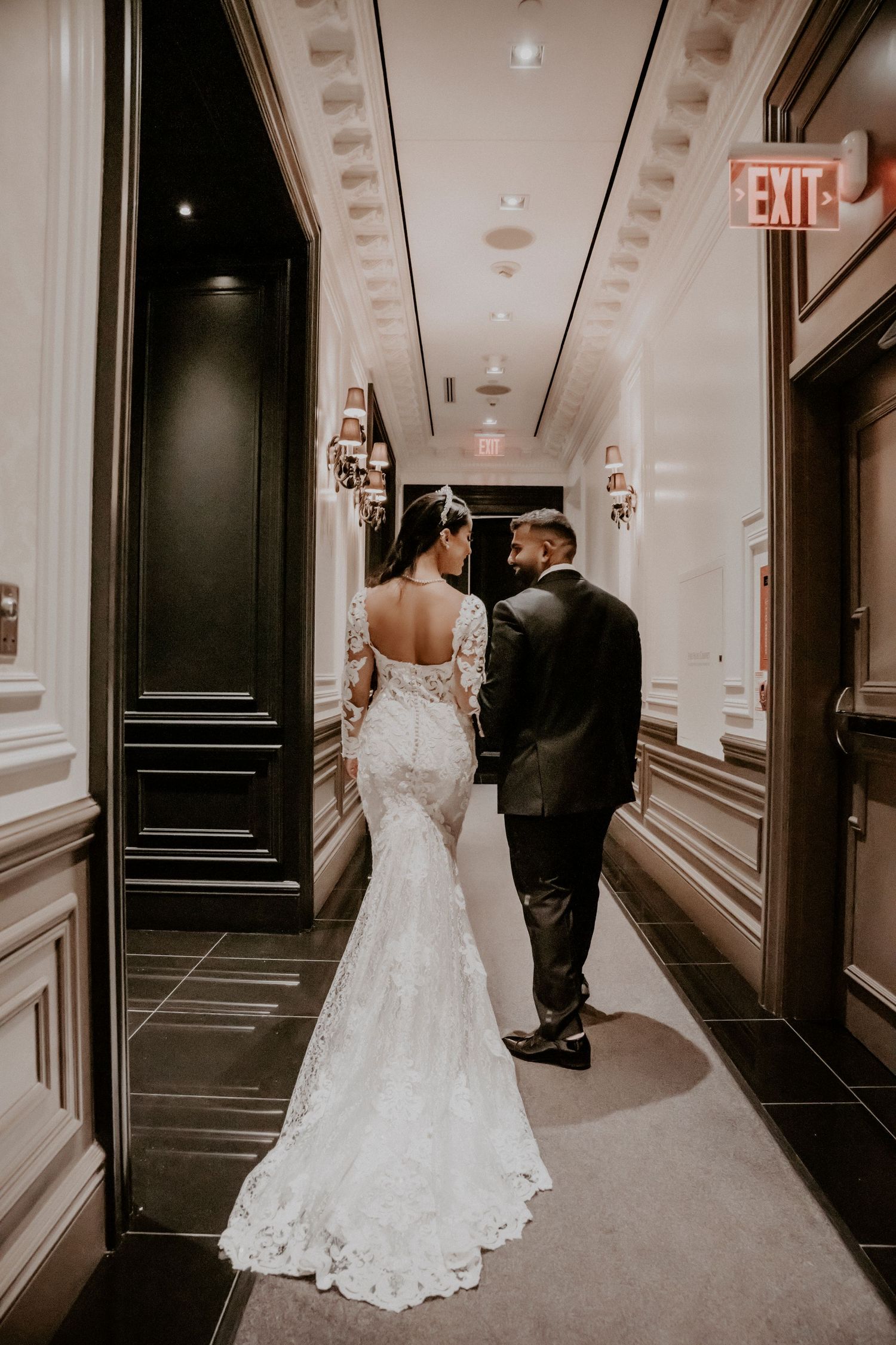Bride and groom walking down elegant hallway showing back of lace wedding dress.