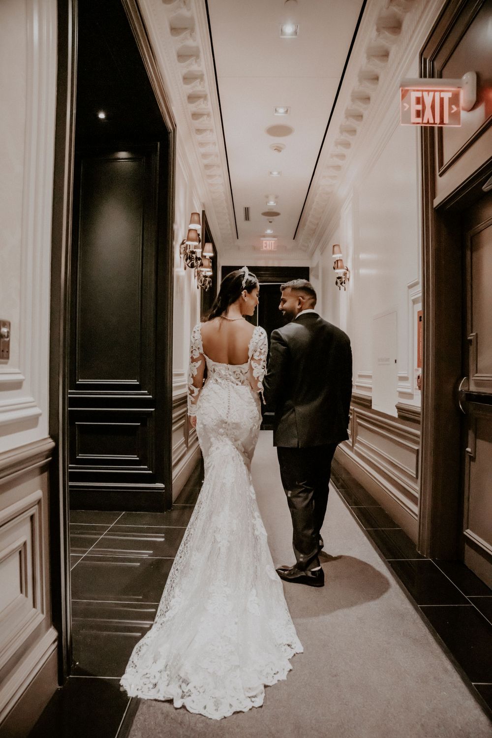 Bride and groom walking down elegant hallway showing back of lace wedding dress.
