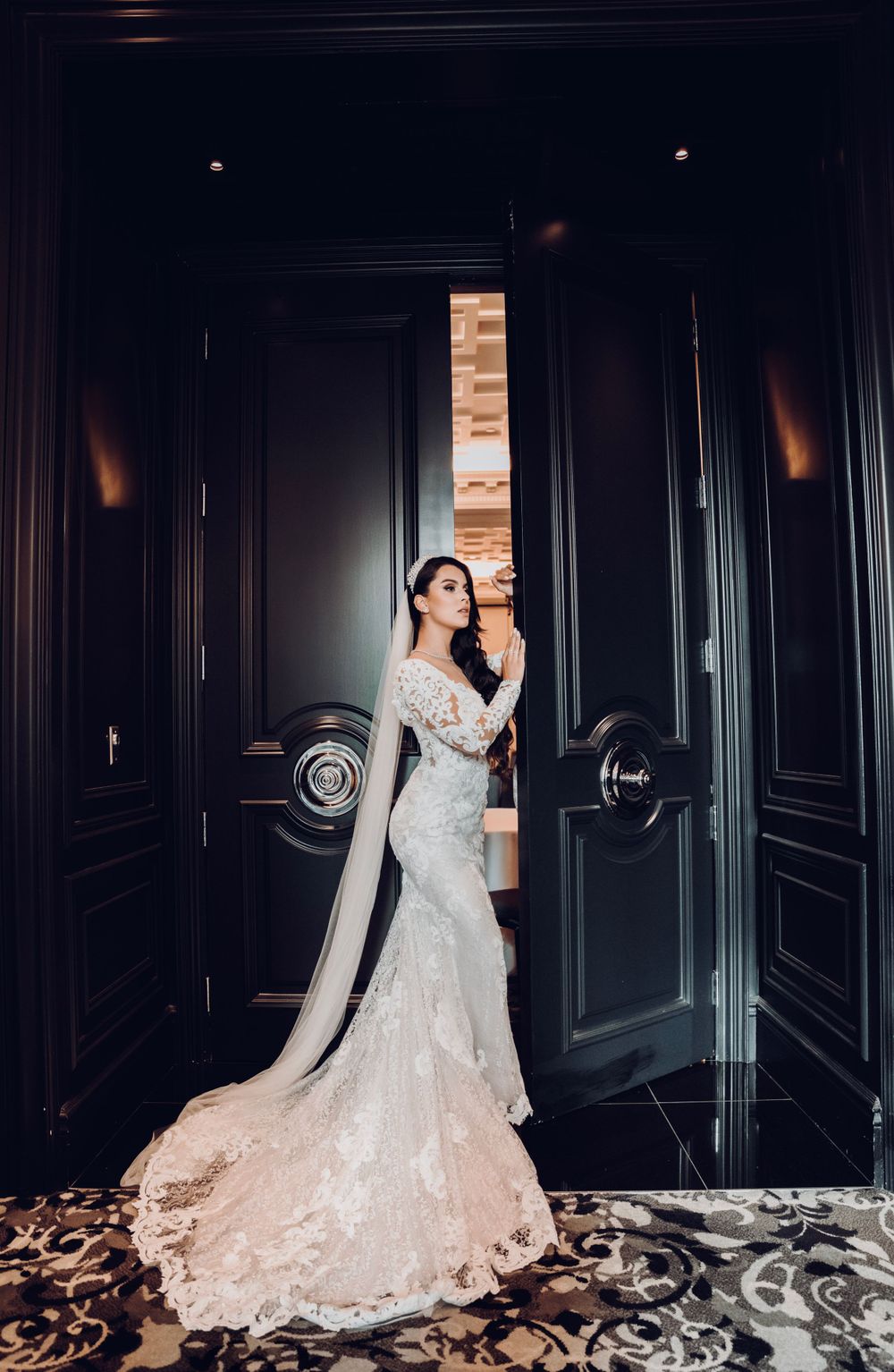 Dramatic portrait of bride in fitted lace gown with cathedral veil against dark doorway.