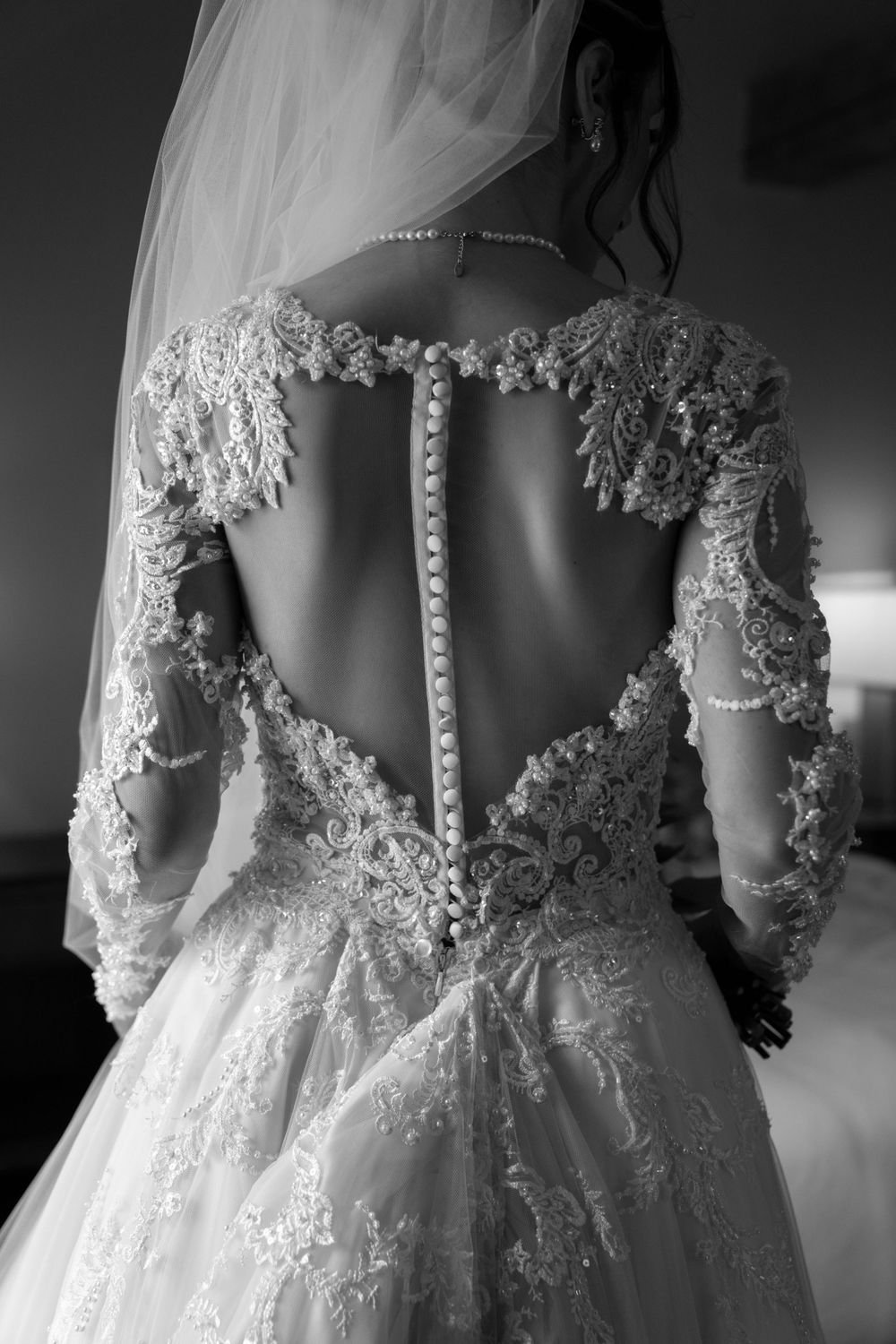 Back view of wedding gown showing intricate lace details and button closure in black and white.