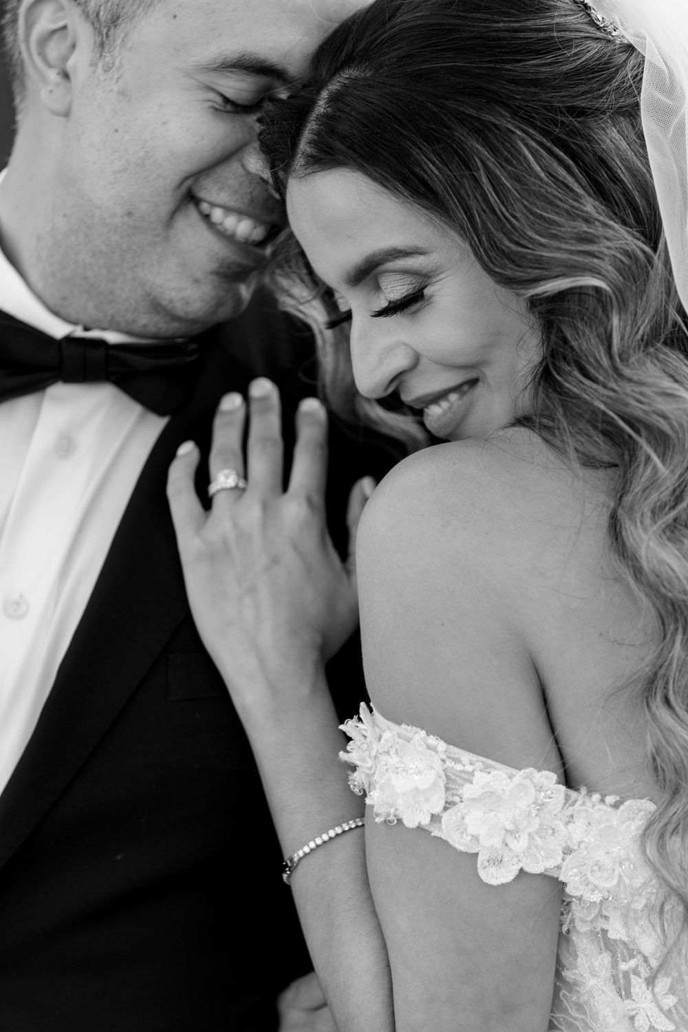 Intimate black and white portrait of newlyweds sharing tender moment in formal wedding attire.