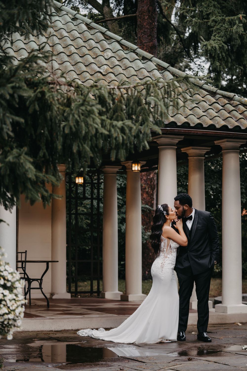 Couple shares a romantic moment under a columned gazebo on their rainy wedding day.
