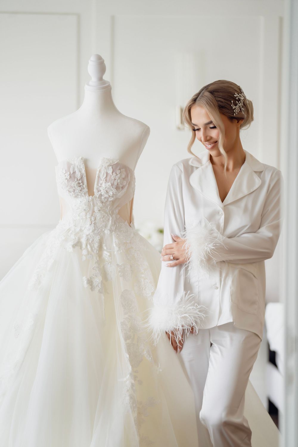 White wedding gown on mannequin next to smiling woman in silk pajamas.