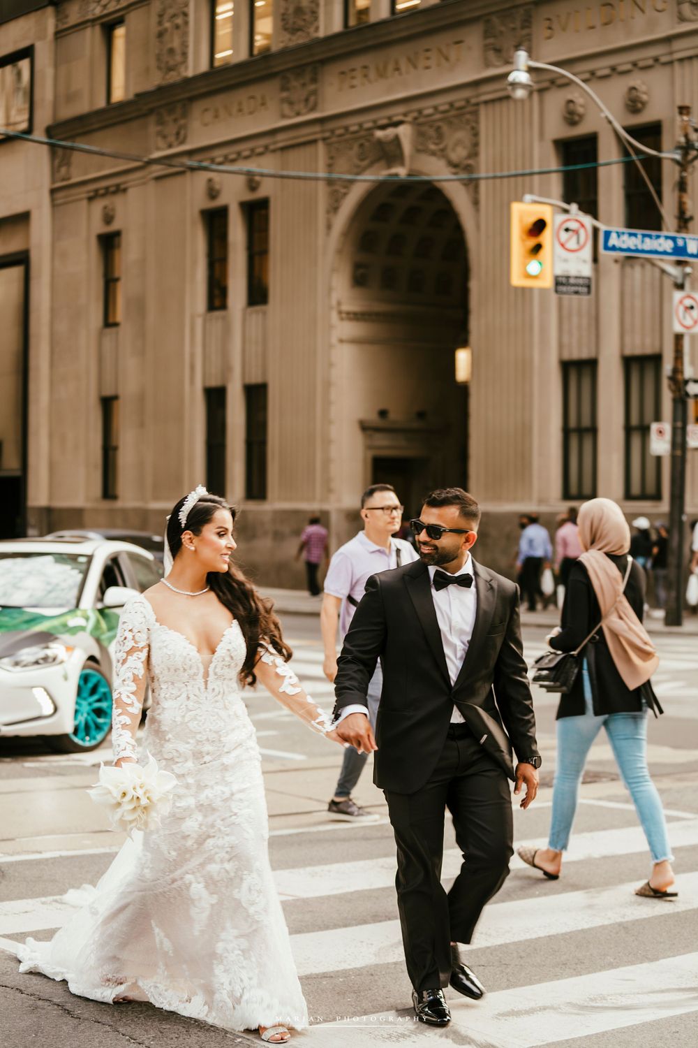 Newlyweds crossing urban street intersection in full wedding attire during downtown photoshoot.