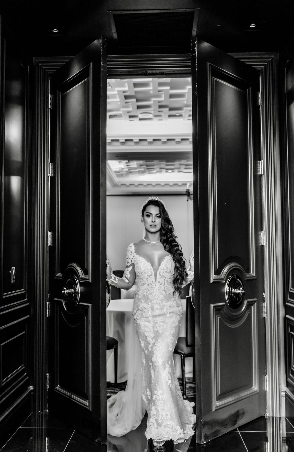 Dramatic black and white bridal portrait through doorway showing lace wedding gown.