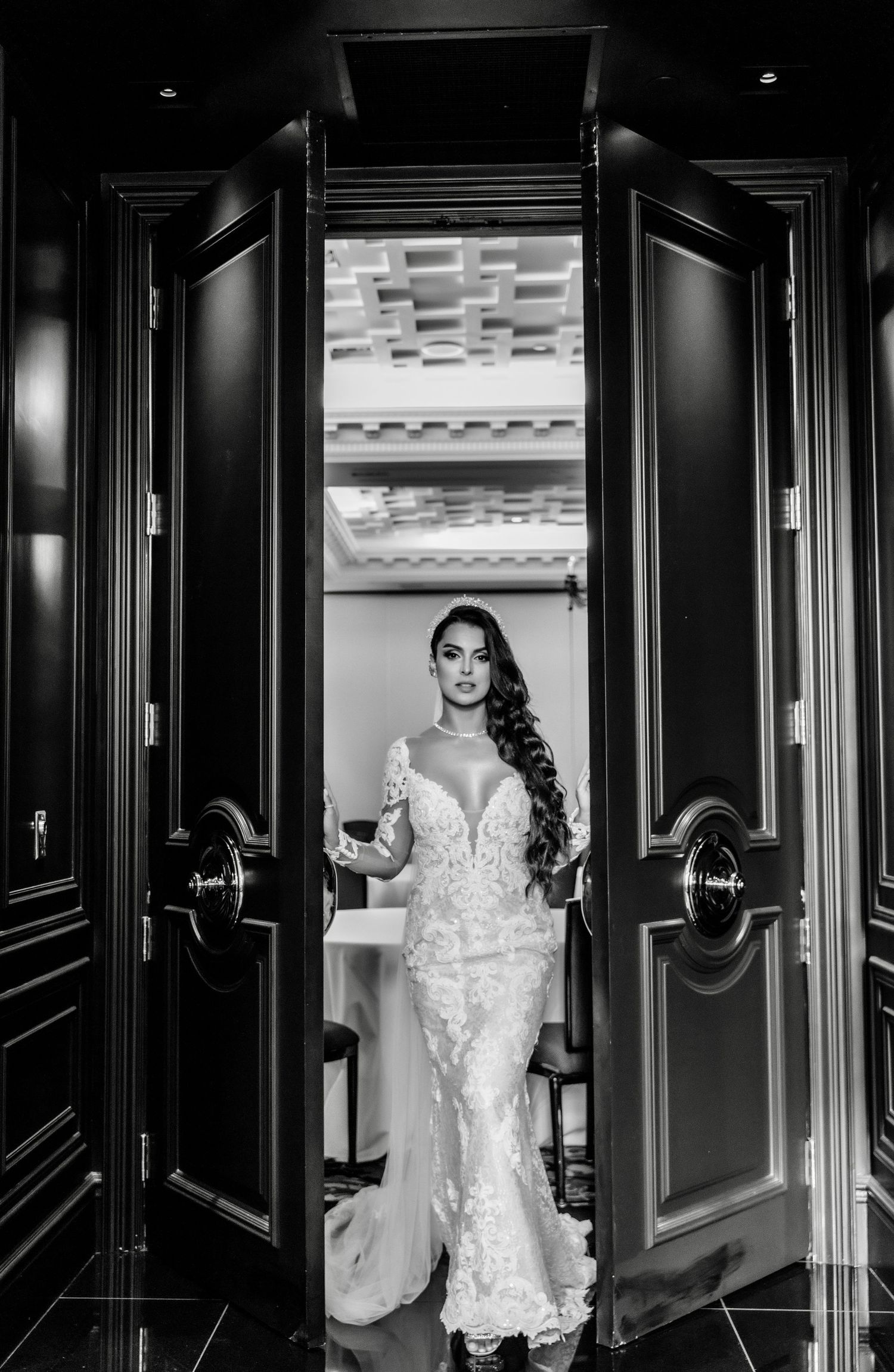 Dramatic black and white bridal portrait through doorway showing lace wedding gown.