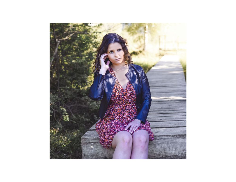 Someone in a blue jacket and floral dress seated on a wooden boardwalk.