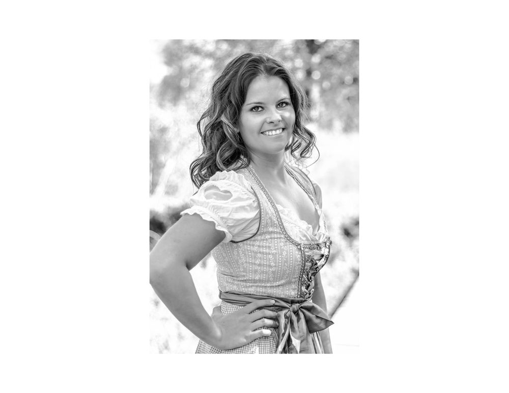A black and white portrait of someone wearing a traditional dirndl dress outdoors.