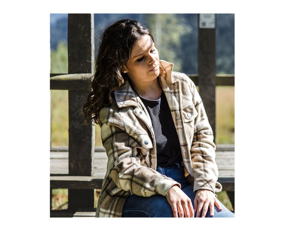 A casual outdoor portrait showing someone in a plaid jacket against a scenic mountain backdrop.