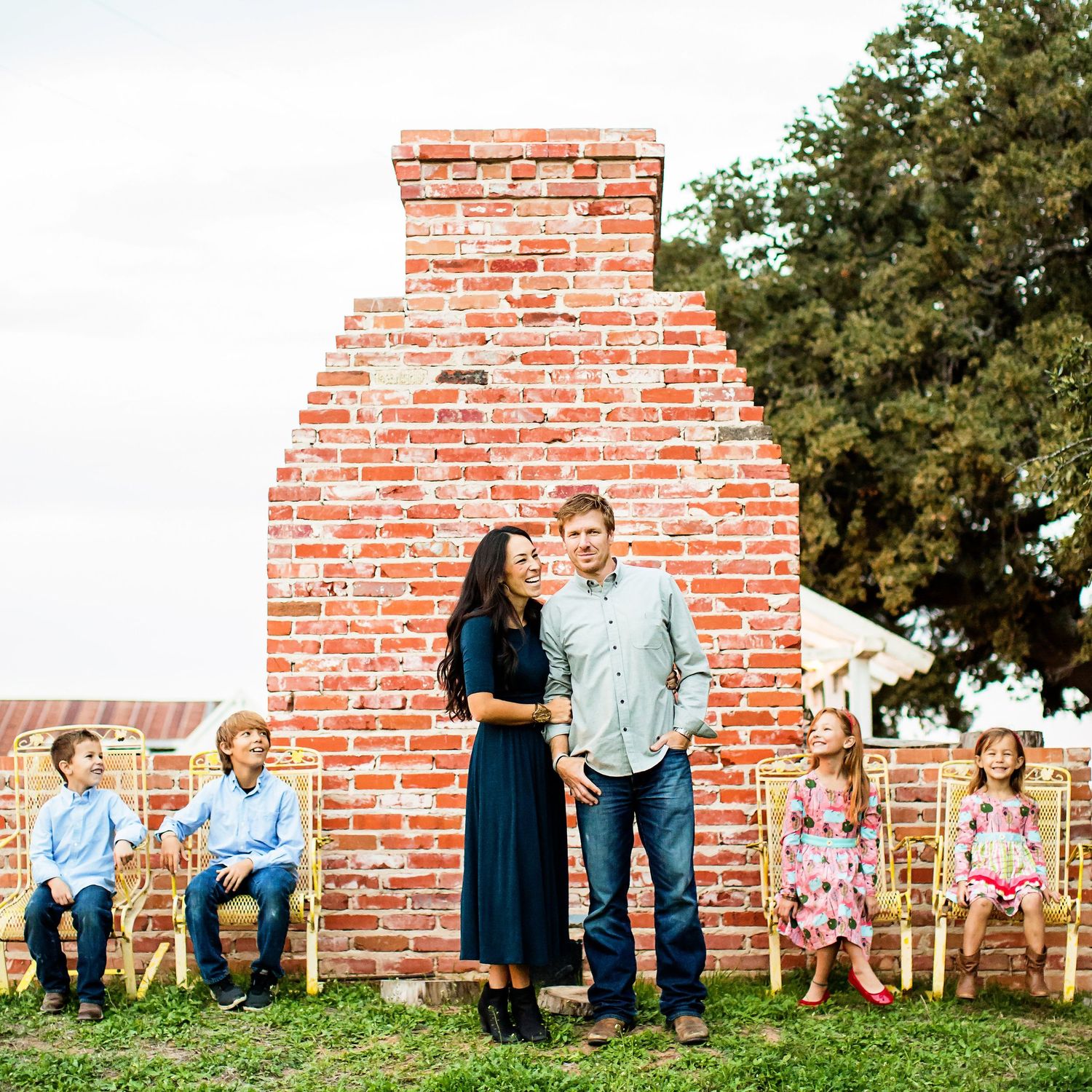 Family portrait against brick wall with children sitting on rustic bench outdoors.