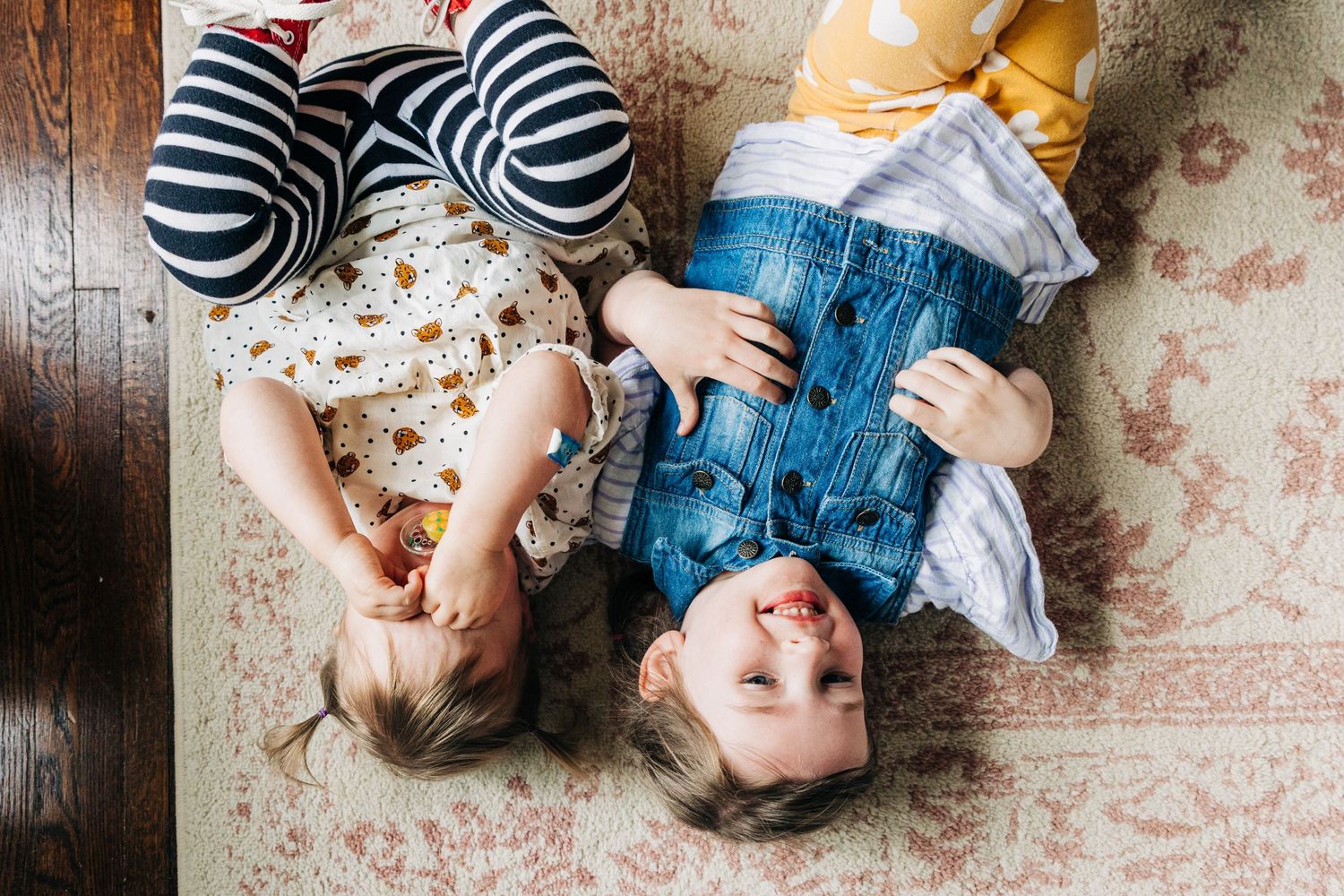 A toddler and her big sister lay on their back on the floor of their Charlotte home.