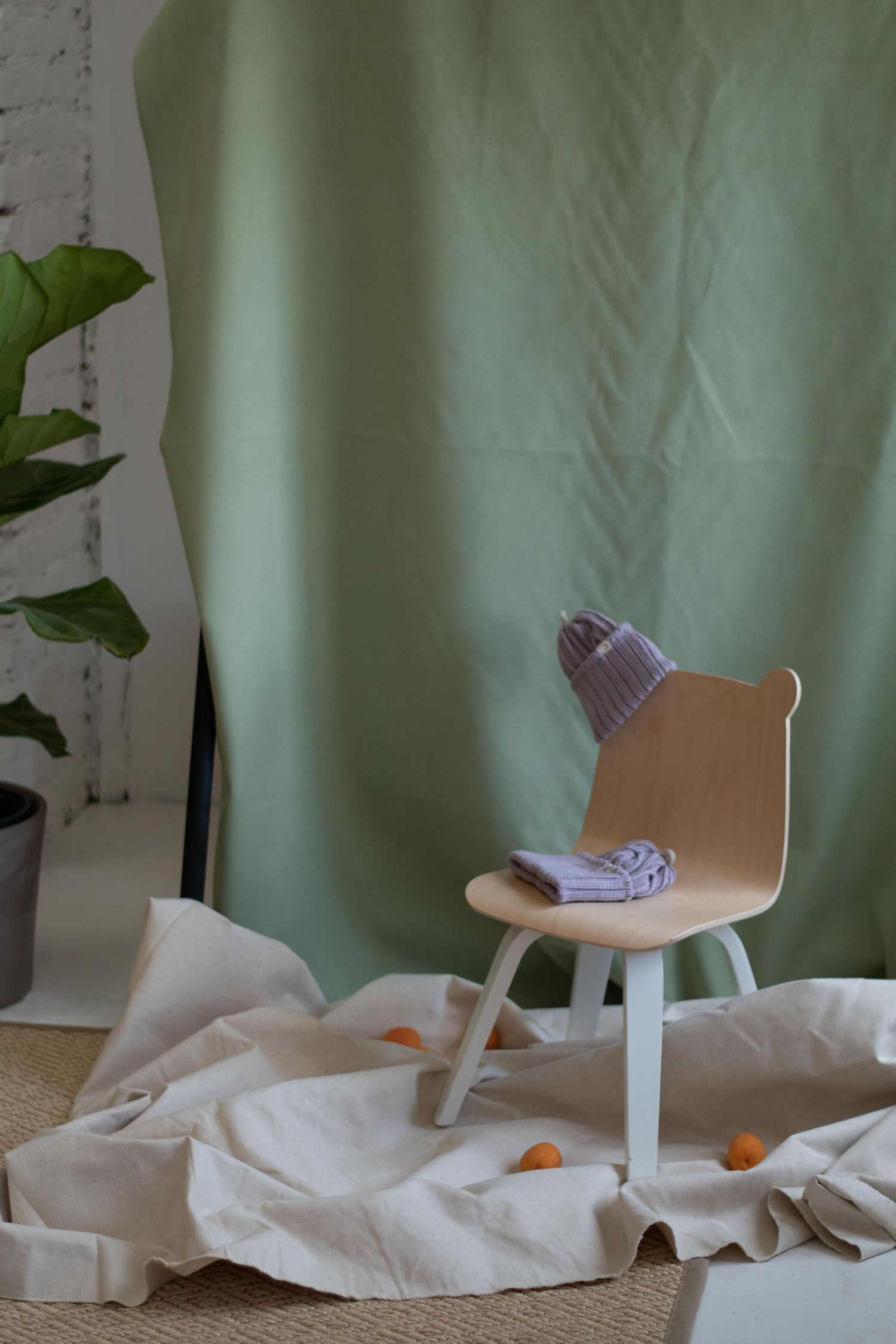 A modern wooden chair with lilac knit hat and white fabric backdrop.