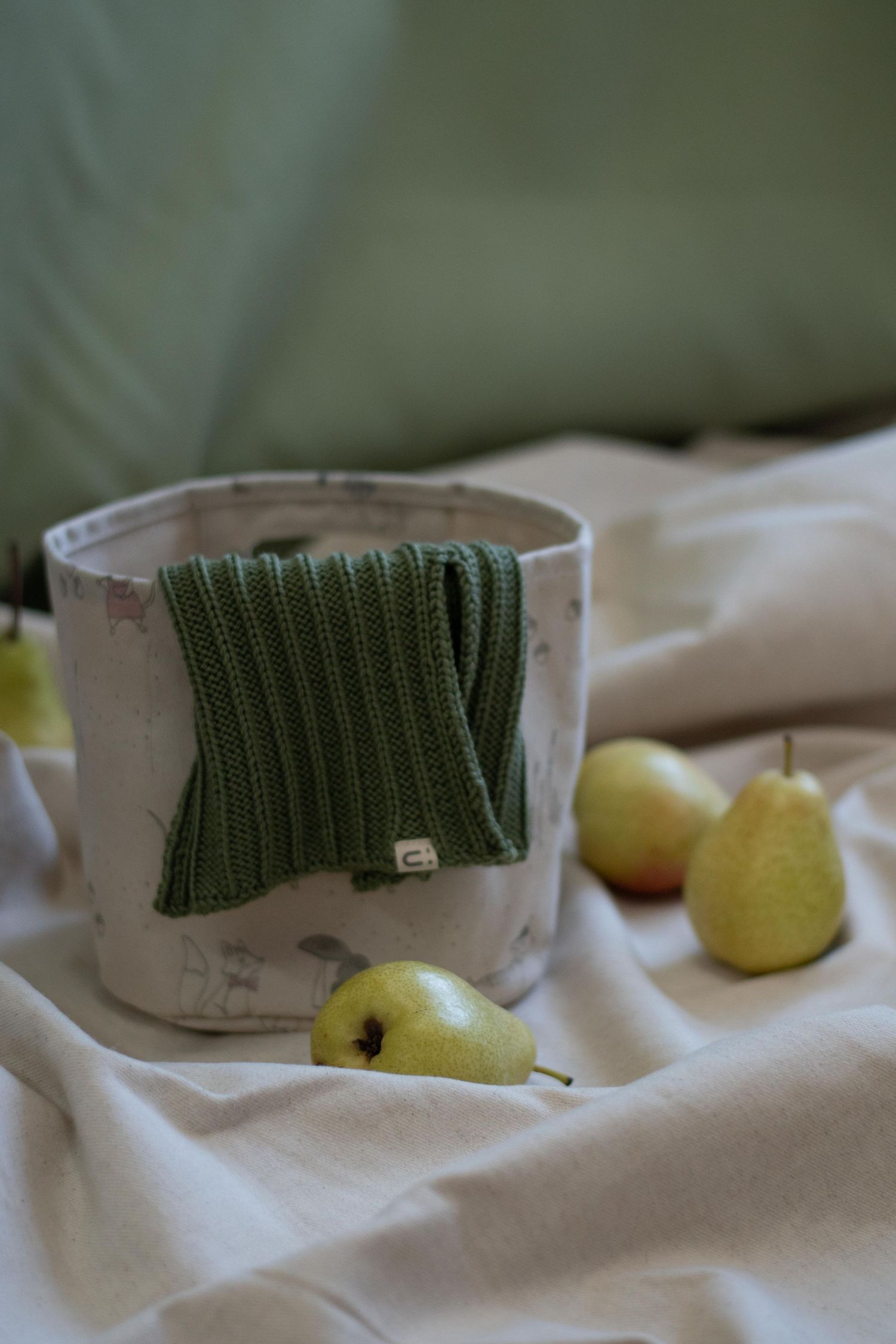 Forest green knit fabric draped over ceramic vessel with fresh pears.