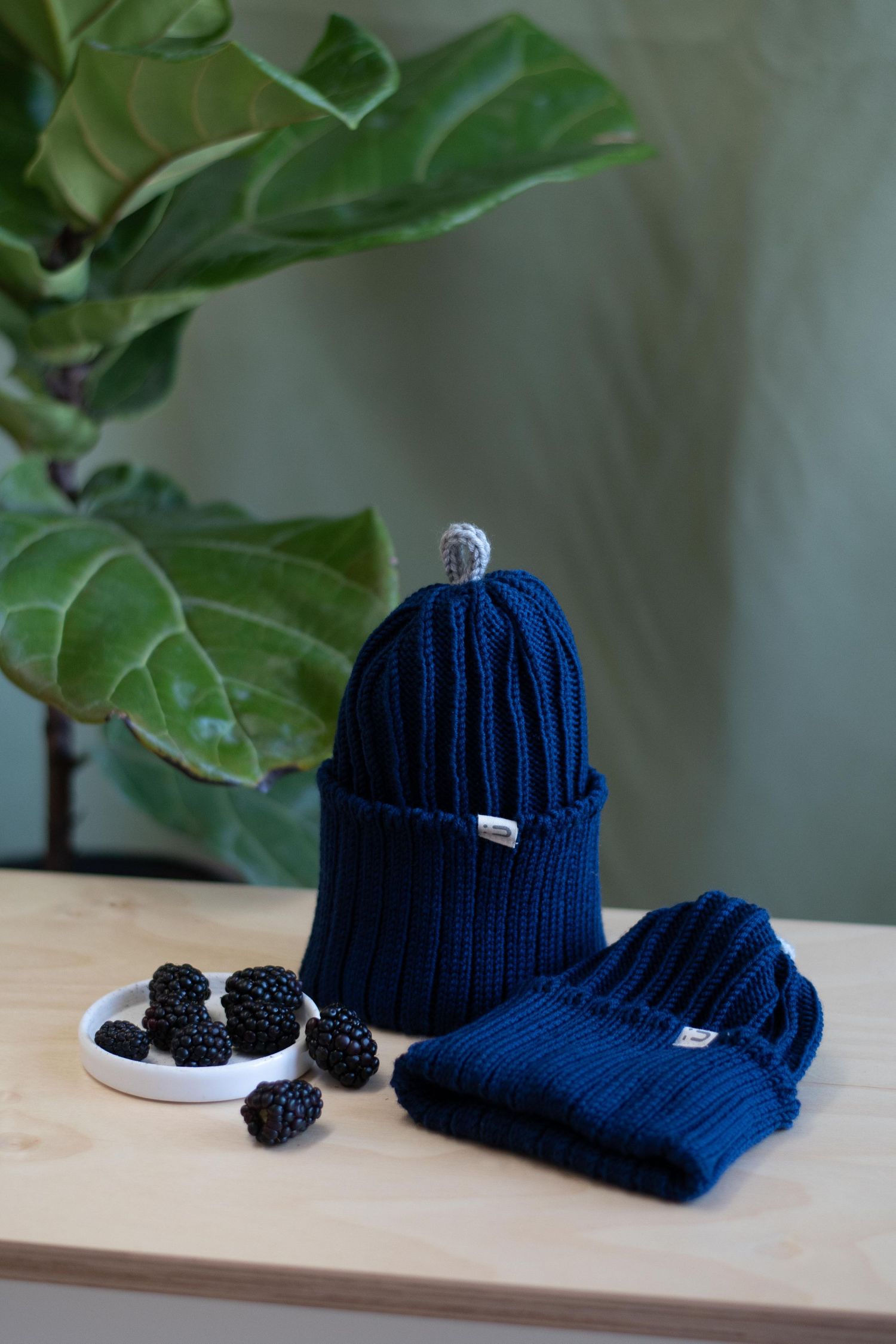 Navy blue knit beanie and scarf set with fresh blackberries on wooden surface.