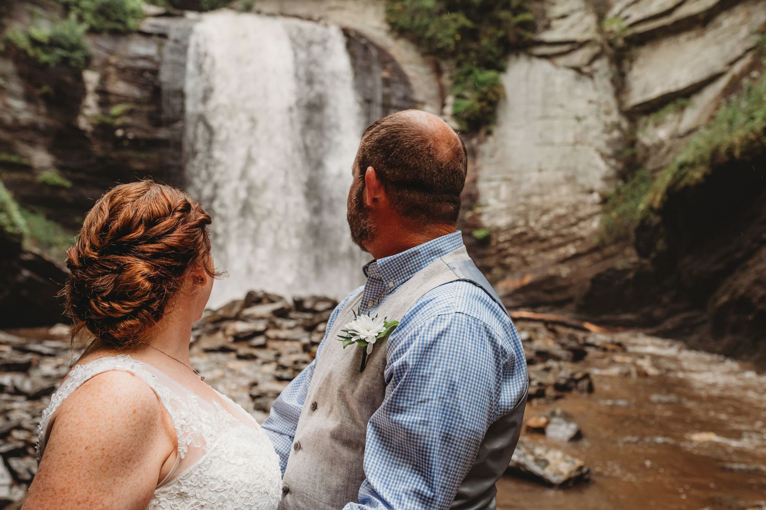 A man and woman face tall waterfall during elopement ceremony in Asheville, NC.