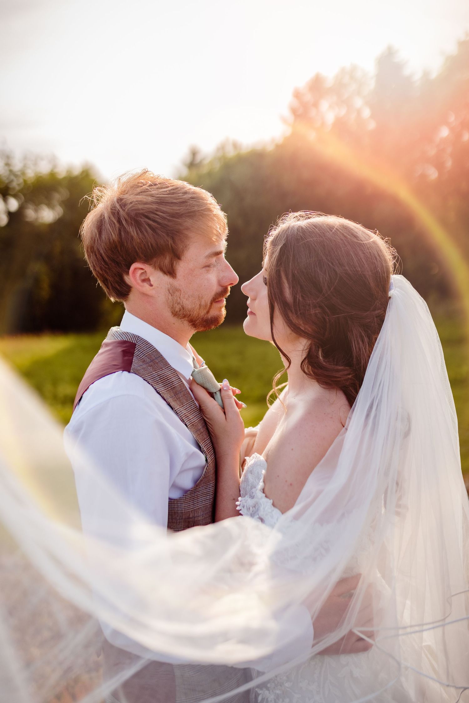 A romantic sunset wedding photo with flowing veil and golden light creating a dreamy atmosphere.