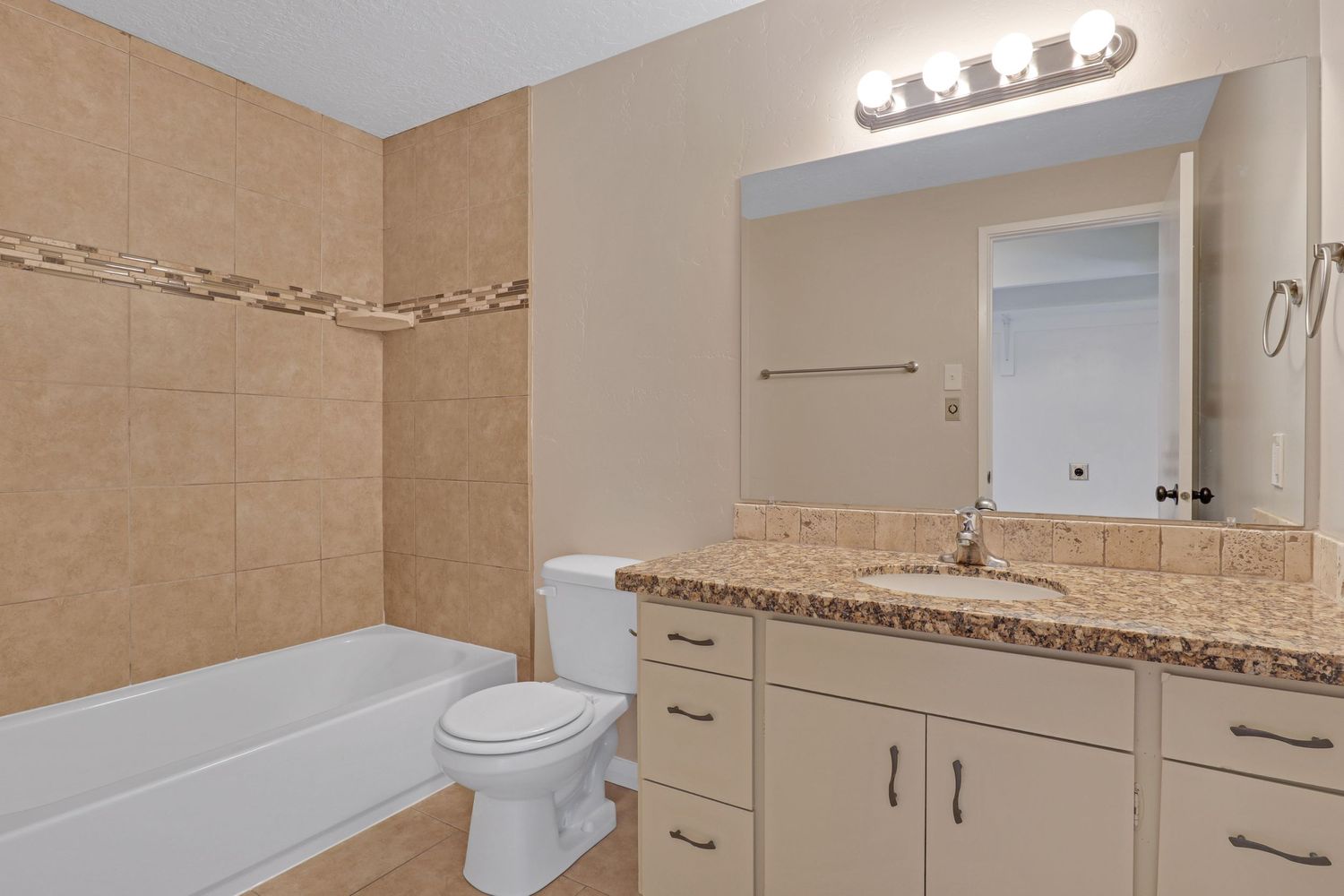 Clean bathroom with tiled tub surround, granite vanity, and white cabinetry.