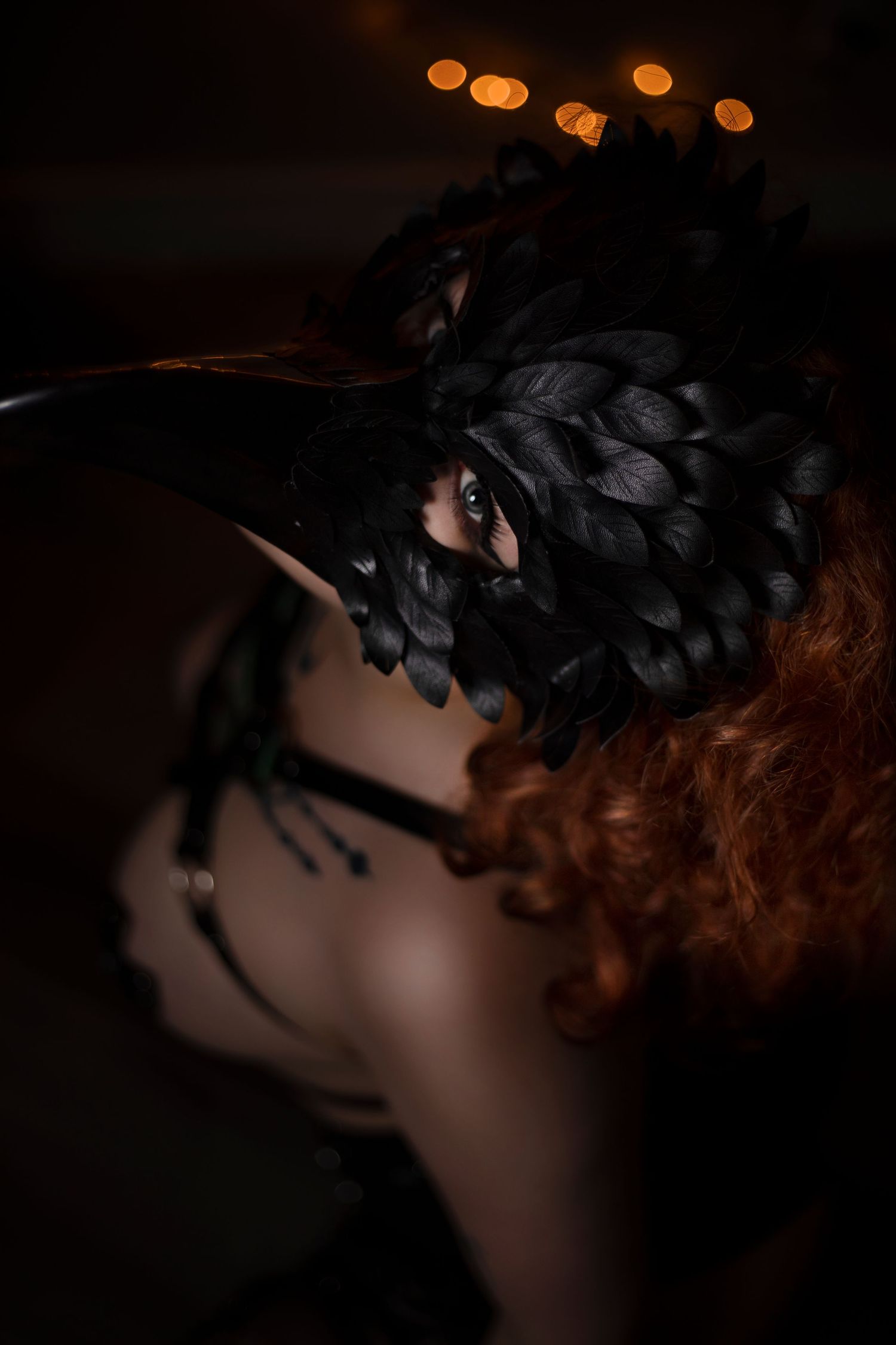 Artistic close-up portrait with black feather details and warm bokeh lighting effects.