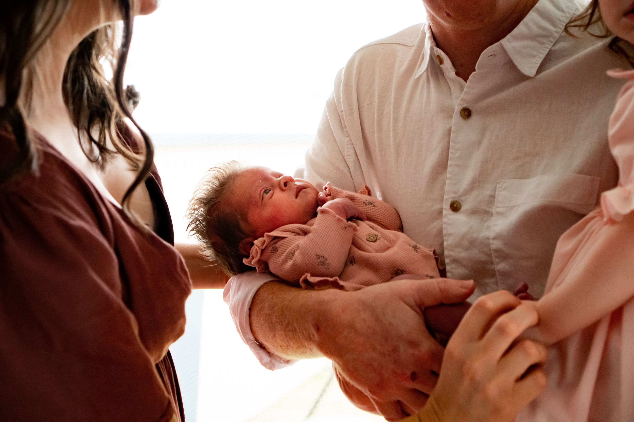 Close up photograph of newborn baby, cradled between mother, father, and sister