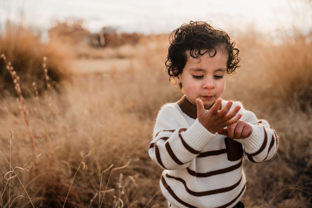 Child in white striped sweater smiles while playing outdoors.