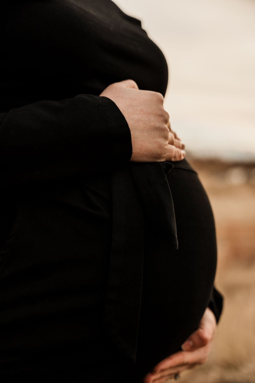 Close-up of hands cradling pregnant belly in black dress.