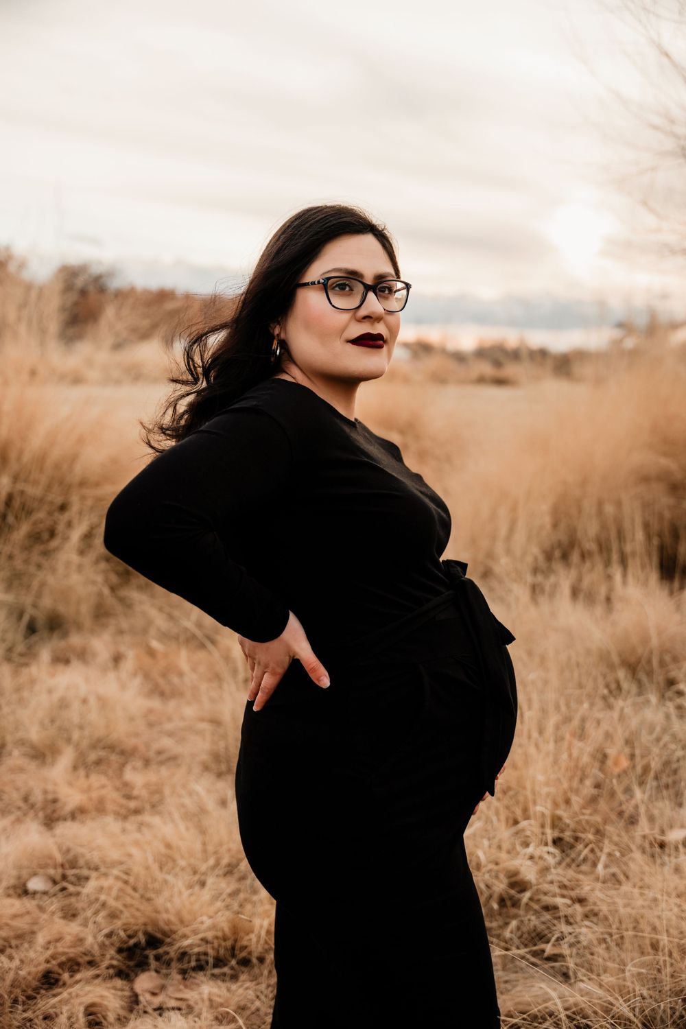 Maternity portrait in black dress against golden autumn field.