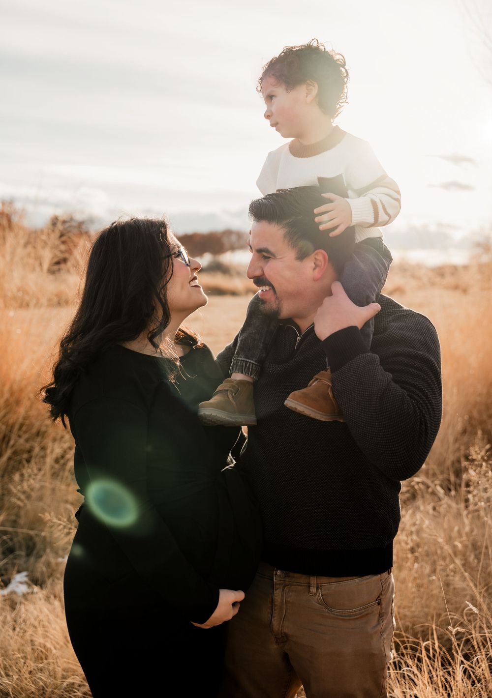 Family embraces in golden light against dried grass landscape during autumn.