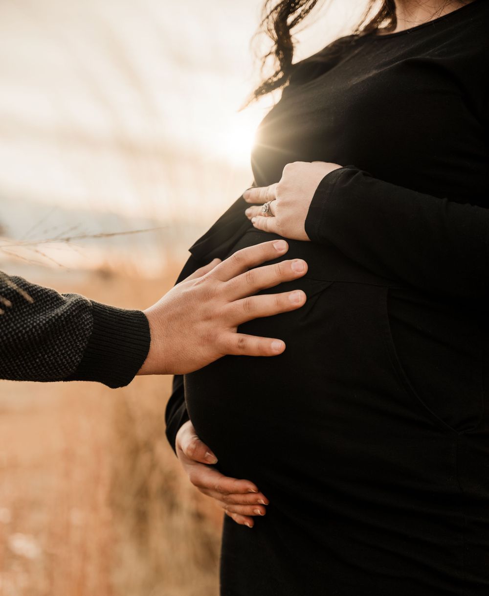 Silhouetted hands tenderly touching a pregnant belly at sunset.