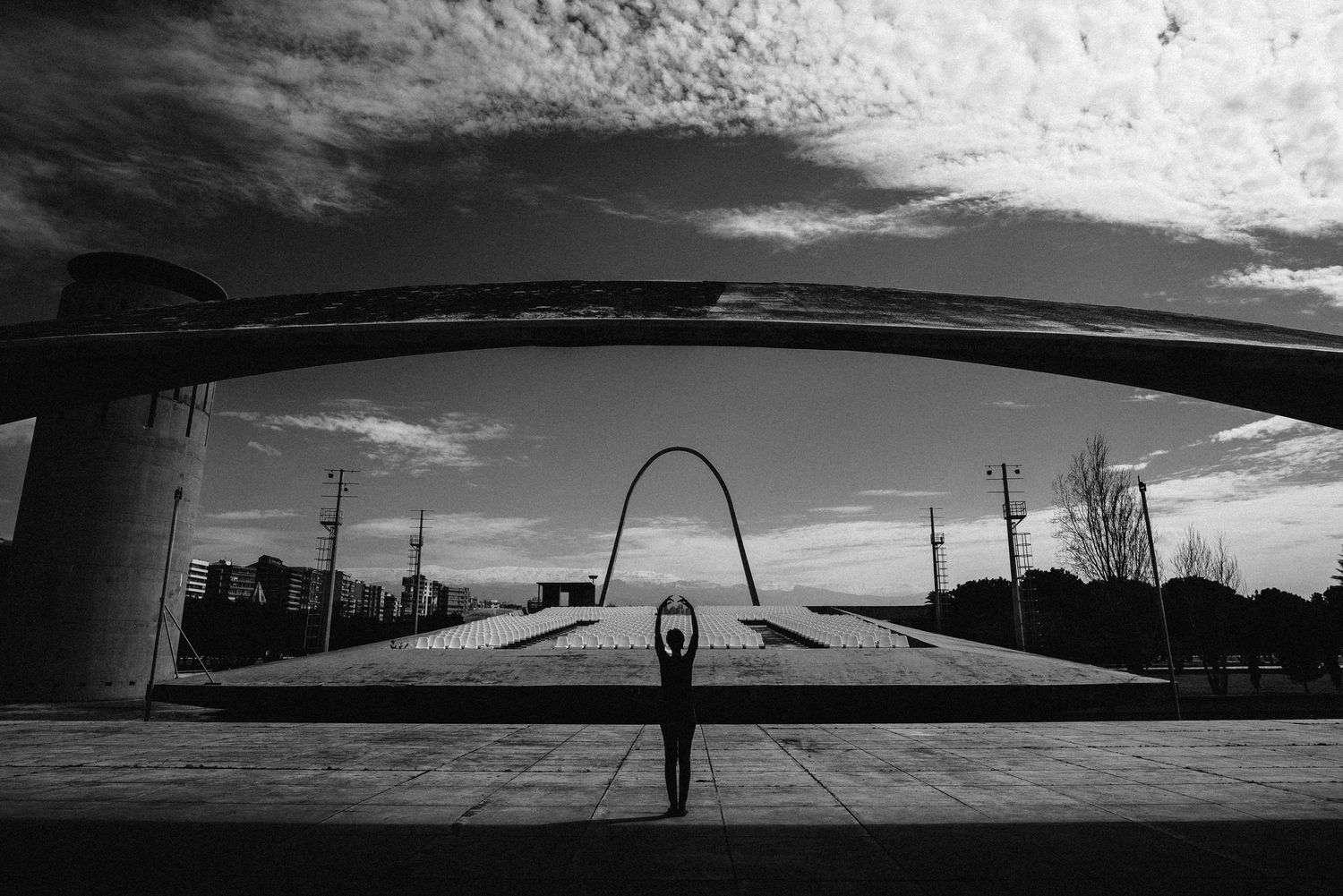 Silhouette under an overpass bridge creating symmetrical architectural composition in black and white.