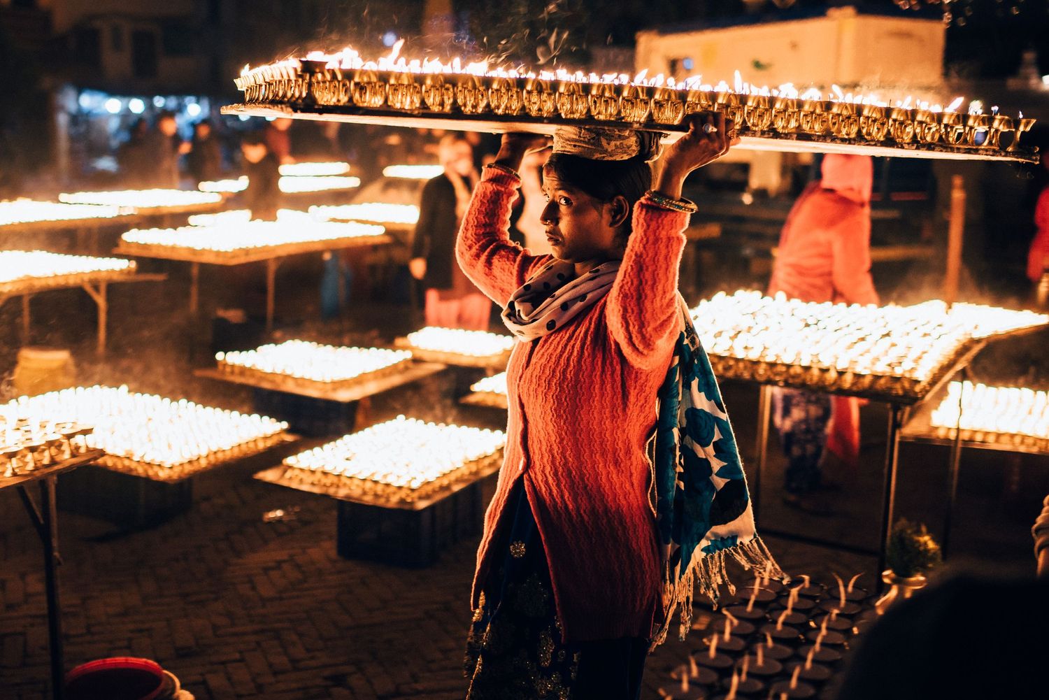 Lighting rows of butter lamps at a Buddhist temple ceremony at night.