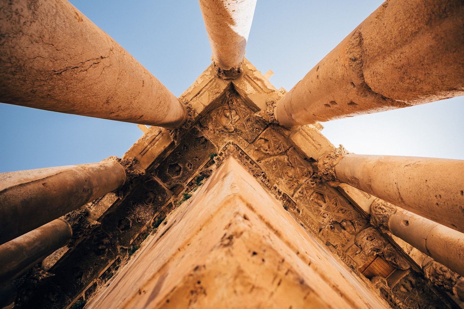 Looking up at converging architectural columns against bright blue sky creating geometric patterns.