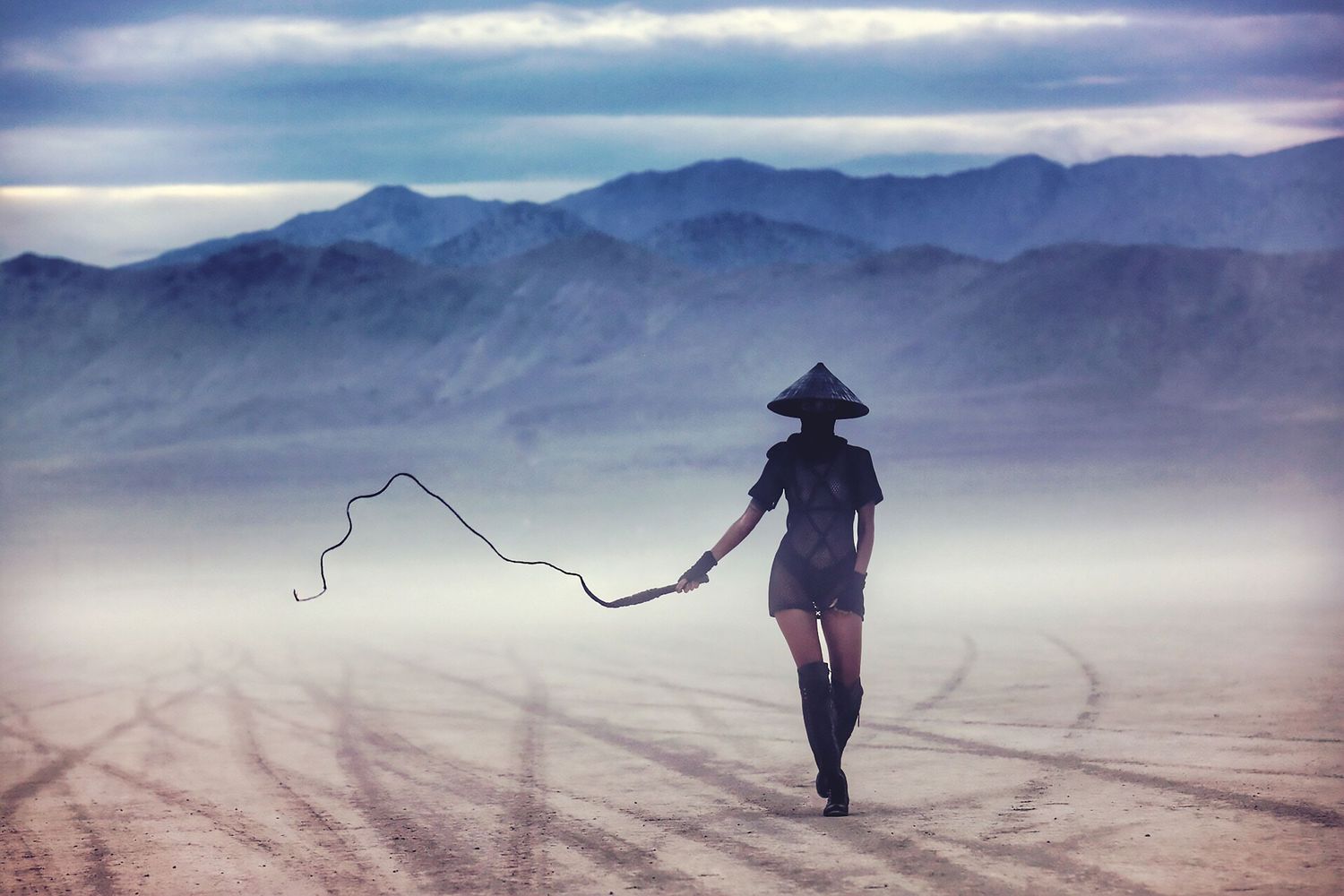 A silhouetted figure in a wide-brimmed hat walks through misty desert landscape pulling a rope in ethereal light. Samurai at Burning Man