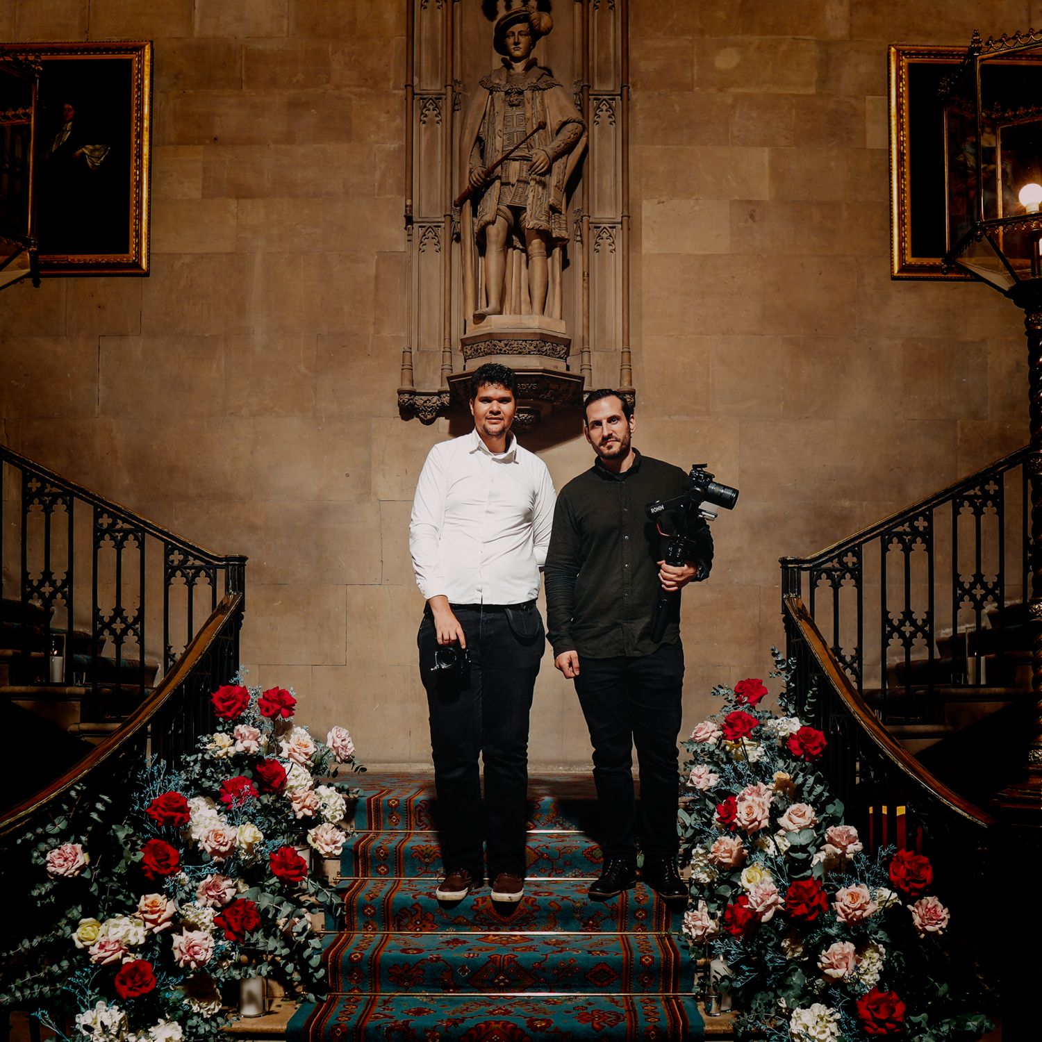 Two people stand on grand staircase decorated with red and white floral arrangements.